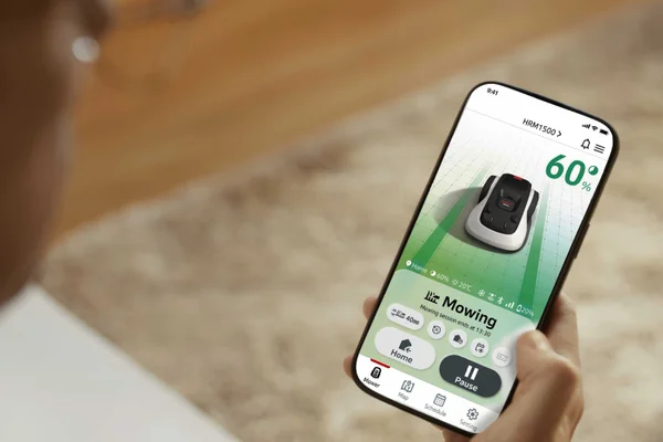 Hand holds phone with mower app, battery at 60% and controls for home and pause.